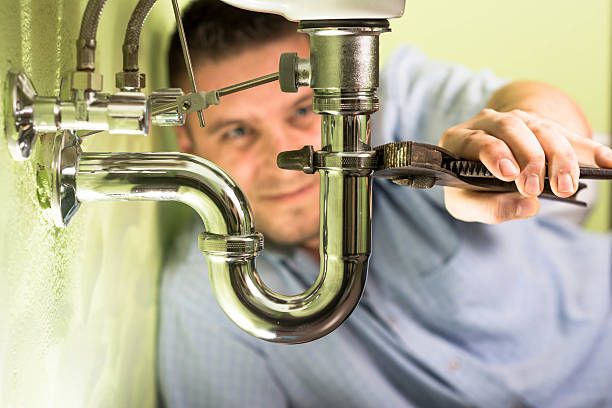 Plumber using a wrench to tighten a siphon under a sink.