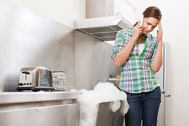 A women on call standing beside the sink with a blocked drain and foam flowing out of it.