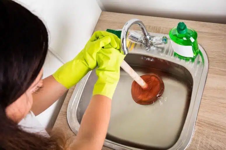 woman clearing a clogged drain with the help of a plunger