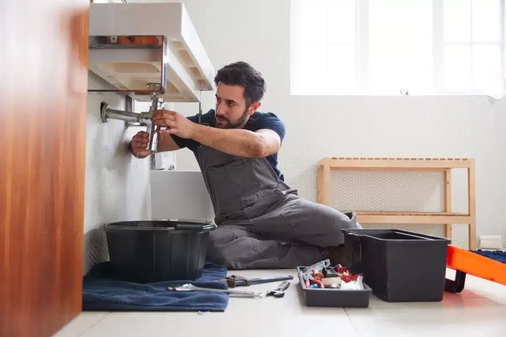 The plumber mending the sink while sitting on the floor